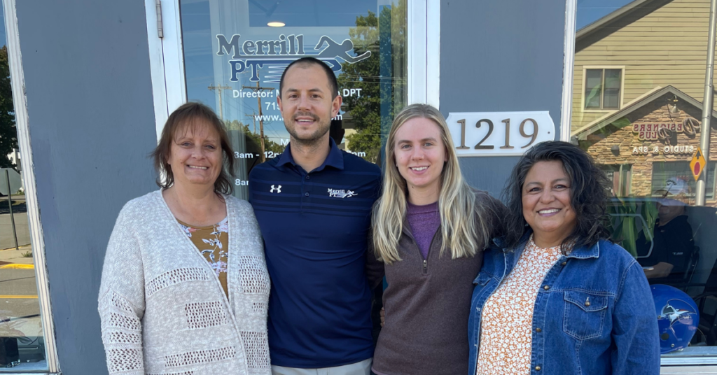 Image of the Merrill PT team: Stacy, Receptionist, Mike Mathson, DPT, Ashley Butalla, Physical Therapist, and Dee Tesch, Assistant, gathered together, ready to provide exceptional care and support to patients.