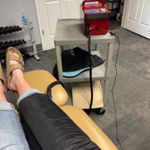 Patient receiving Game Ready therapy at Merrill PT for knee surgery recovery. The device is wrapped around the knee, providing cold compression to reduce swelling and accelerate healing.